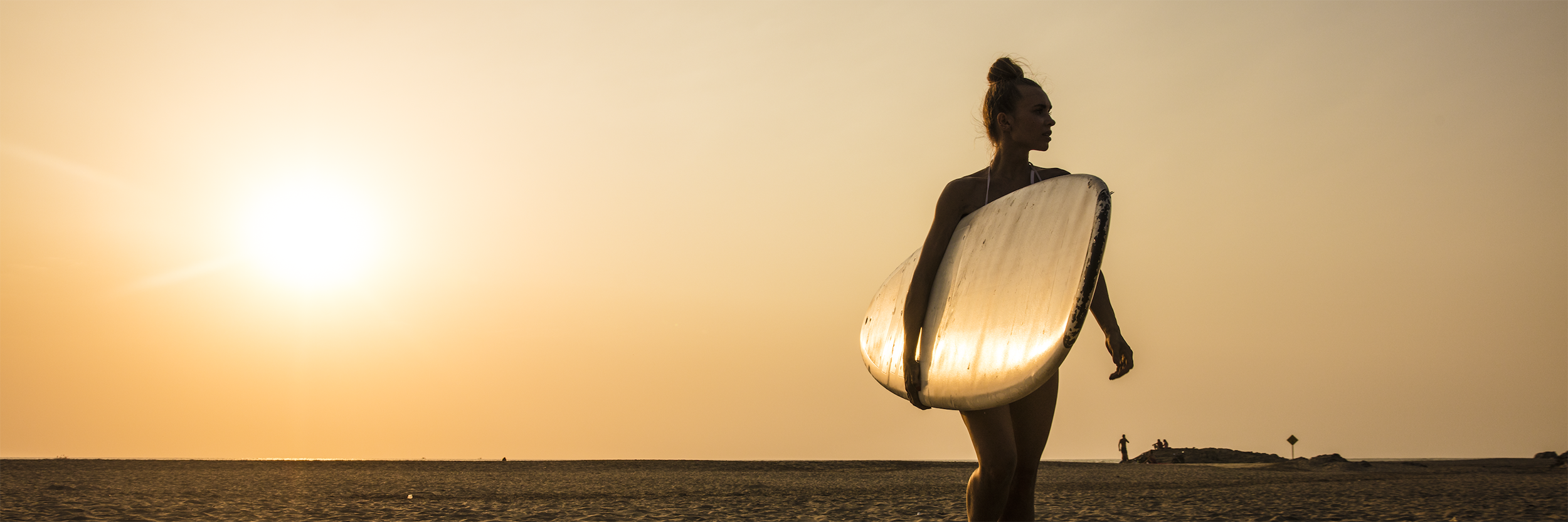 woman on the beach carrying a surf board at sunset